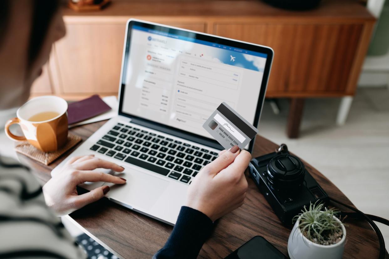 A woman shopping online for flight tickets on airline website with laptop, entering credit card details to make mobile payment at home.