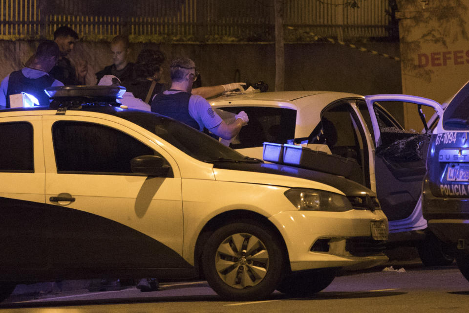 FILE - In this March 14, 2018 file photo, Brazilian police officers work on a crime scene as they stand next to vehicle in which council member Marielle Franco and her driver where both shot to death by two unidentified attackers in Rio de Janeiro, Police in Brazil said on Tuesday, March 12, 2019, that they have arrested two suspects in the killing of Franco and her driver last year. (AP Photo/Leo Correa, File)