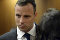 Oscar Pistorius talks to an unidentified person before proceedings get under way in the high court in Pretoria, South Africa, Monday, March 24, 2014. The trial of Pistorius, who is charged with murder for the shooting death of his girlfriend Reeva Steenkamp on Valentines Day in 2013, is beginning its fourth week. The prosecution has said it will wrap up its case against the double-amputee runner this week after calling four or five more witnesses, beginning Monday. (AP Photo/Chris Collingridge, Pool)