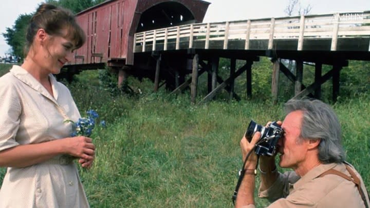 Meryl Streep posing for a photo as Clint Eastwood kneels down to take one in The Bridges of Madison County.