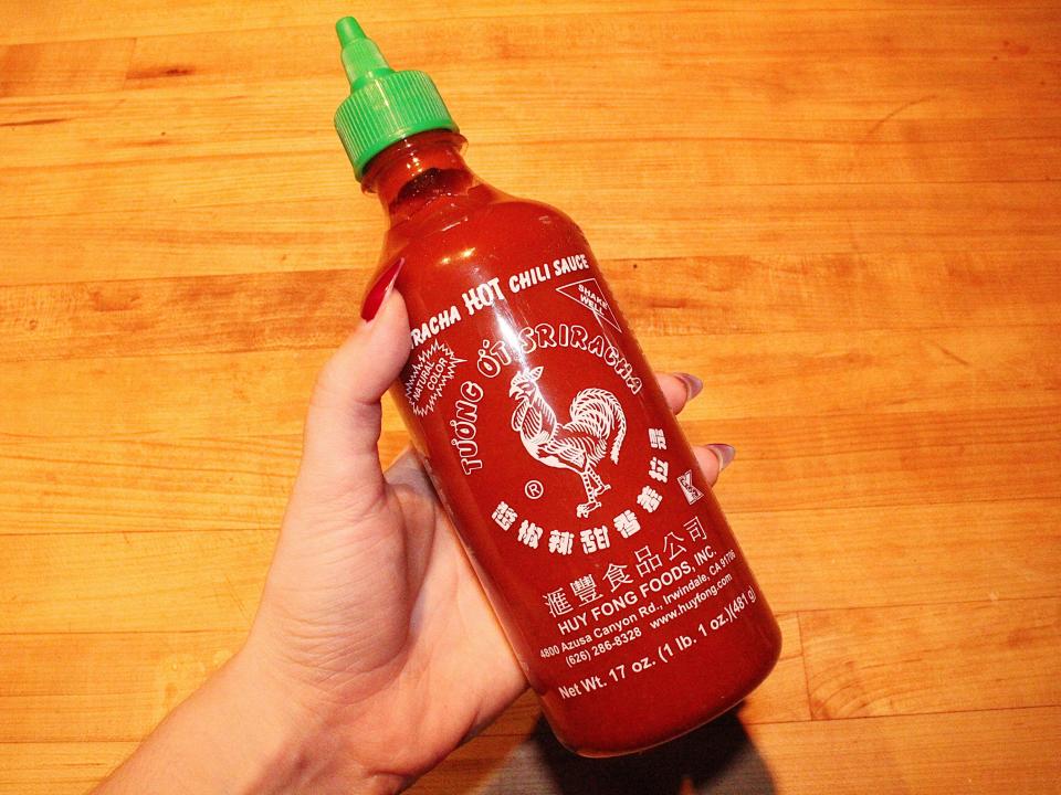 person holding bottle on sriracha on wooden background