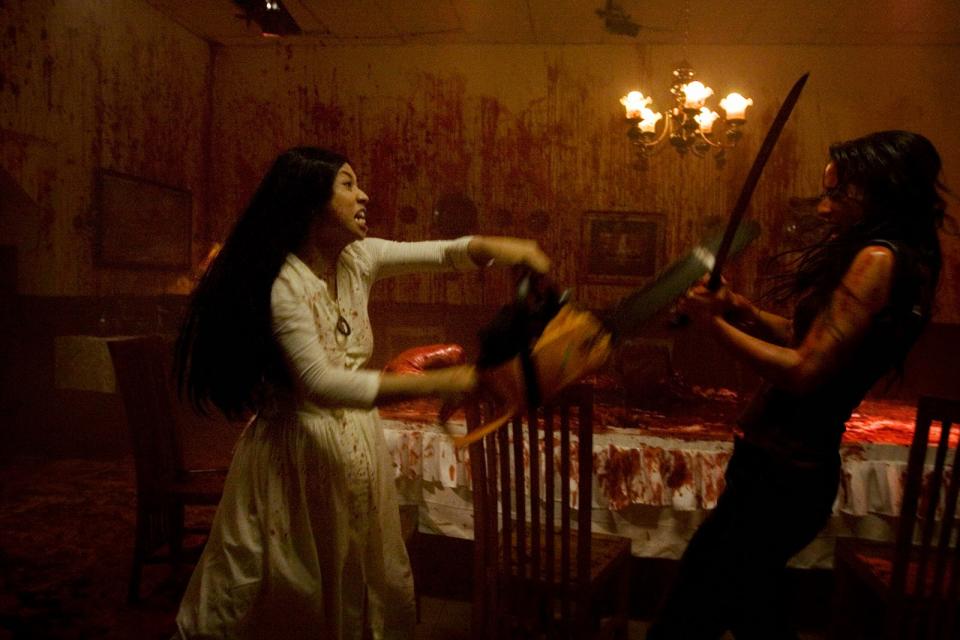 A still from Macabre shows a woman with a chainsaw attacking a woman with a knife in a gore soaked room