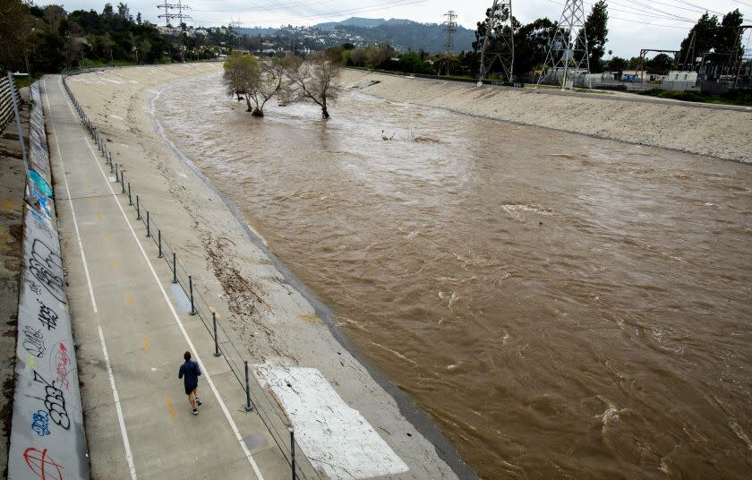 LOS ANGELES, CA - MARCH 16: A jogger runs on the river trail in a view from the Fletcher Drive Bridge crossing a soft-bottom section of the LA River as it flows through Atwater Village where officials say vegetation, debris and trees could cause storm water to back up in the channel and potentially local neighborhoods on Thursday, March 16, 2023 in Atwater Village, CA. (Brian van der Brug / Los Angeles Times)