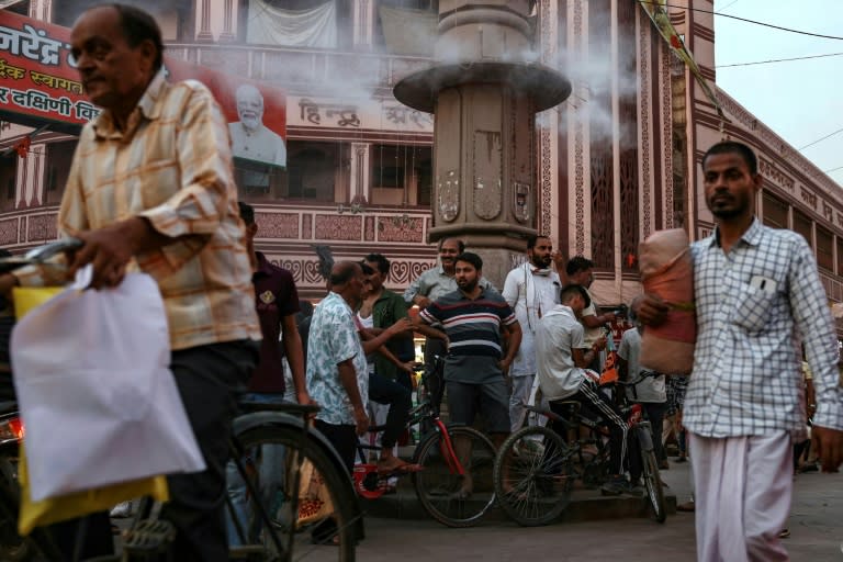 Hombres aguardan junto a un aspersor de agua instalado para refrescar un mercado en la ciudad india de Varanasi, el 31 de mayo de 2024 (Niharika KULKARNI)