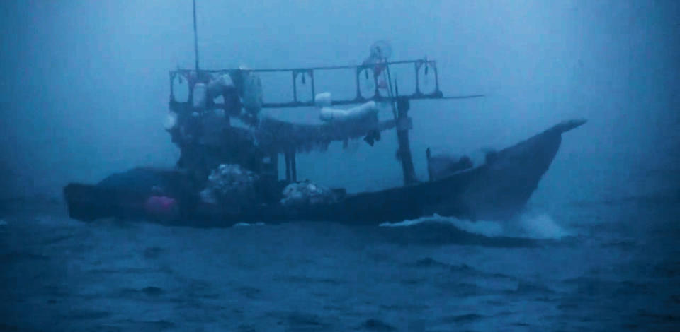 A dimly lit small boat with ragged equipment drifts in choppy waters.