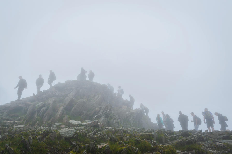 When UK relaxed pandemic lockdown rules in August 2020 it resulted in surge of ''stay-cation holidays''. Hikers awaits in a queue on foggy and misty day for their turn to access the peak of mount Snowdon to take a selfie.