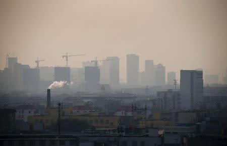 Smoke rises from a chimney among houses as new high-rise residential buildings are seen under construction on a hazy day in the city centre of Tangshan, Hebei province in this February 18, 2014 file photo. REUTERS/Petar Kujundzic/Files