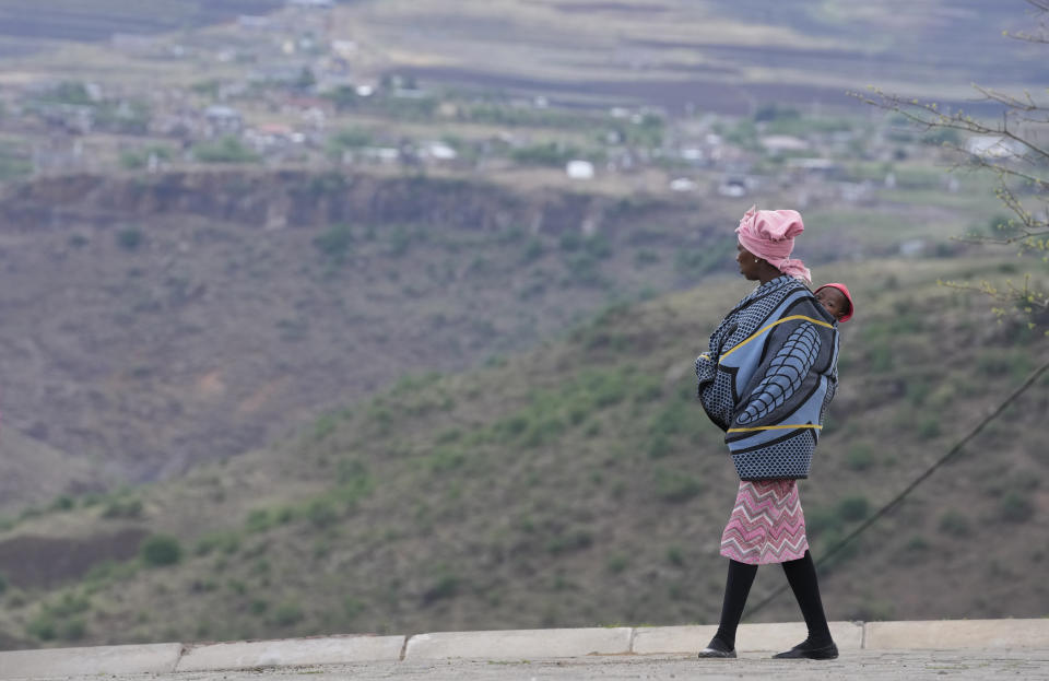 A woman carrying a child stands outside a polling station in Thaba-Tseka District, 82km east of Maseru, Lesotho, Friday, Oct. 7, 2022. Voters across Lesotho are heading to the polls Friday to elect a leader to find solutions to high unemployment and crime. (AP Photo/Themba Hadebe)