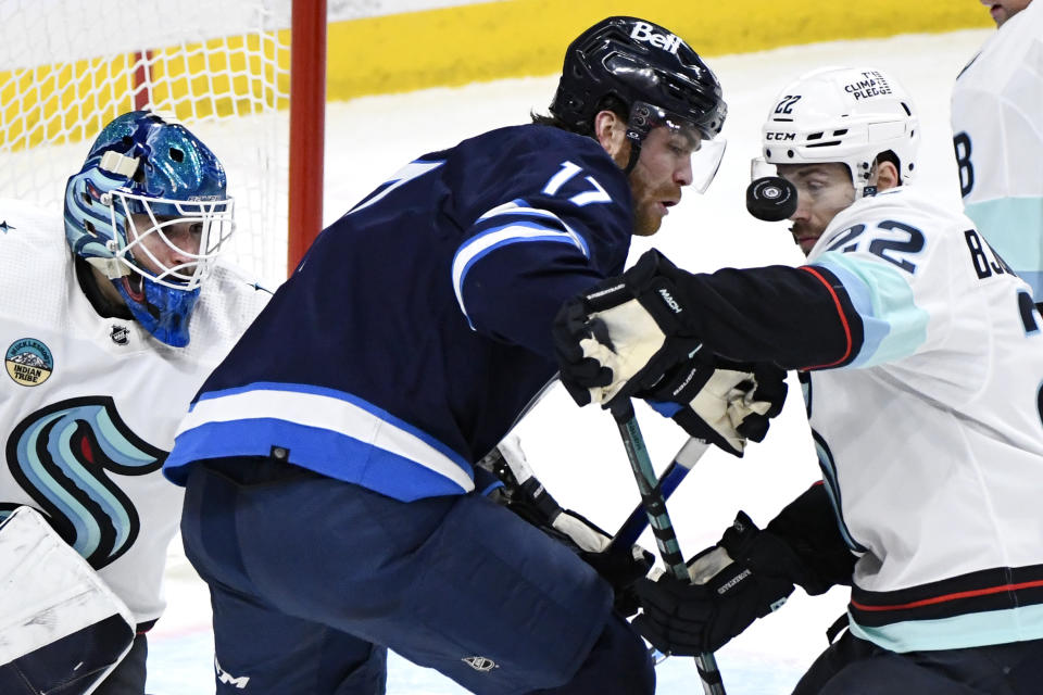 Seattle Kraken's Oliver Bjorkstrand (22) and Winnipeg Jets' Adam Lowry (17) compete for the puck during the third period of an NHL hockey game Tuesday, March 5, 2024, in Winnipeg, Manitoba. (Fred Greenslade/The Canadian Press via AP)