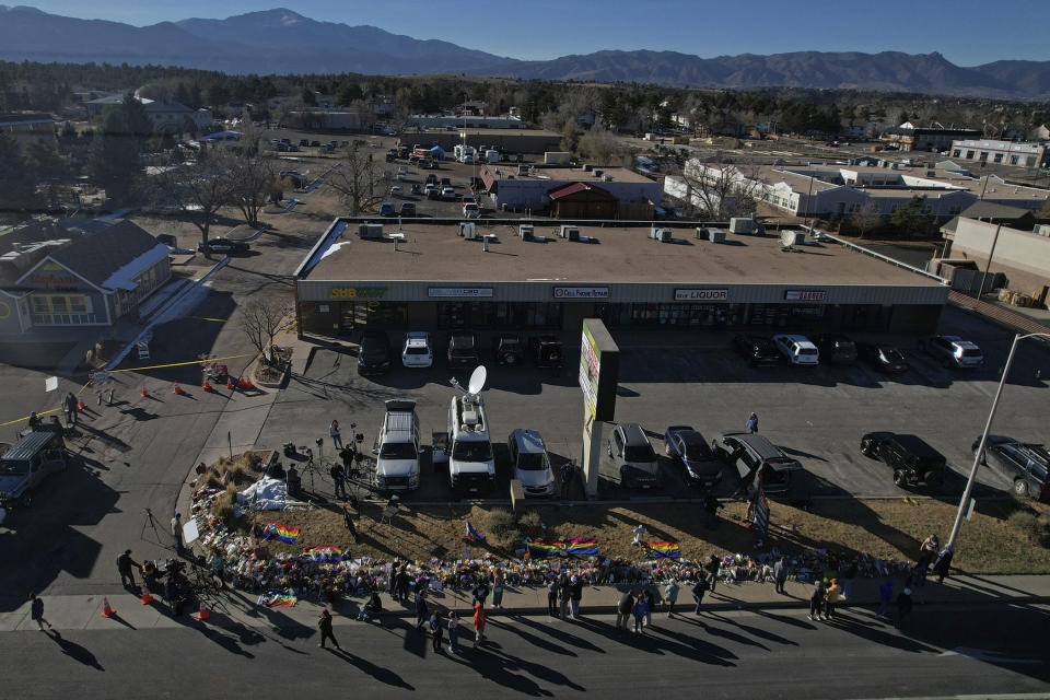 People visit a makeshift tribute with a display of flowers and flags on a corner near the site of a mass shooting at a gay bar Monday, Nov. 21, 2022, in Colorado Springs, Colo. (AP Photo/Brittany Peterson)