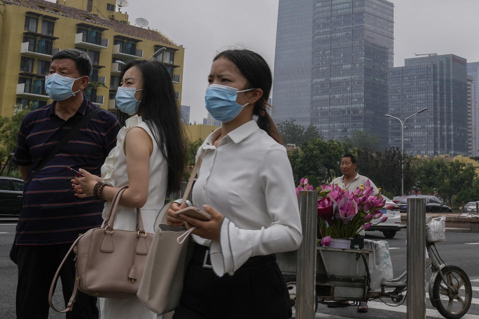 People wearing face masks to help curb the spread of the coronavirus stand watch near a vendor selling flowers outside a subway station in Beijing, Thursday, July 22, 2021. A senior Chinese health official says China cannot accept the World Health Organization's plan for the second phase of a study into the origins of COVID-19. (AP Photo/Andy Wong)