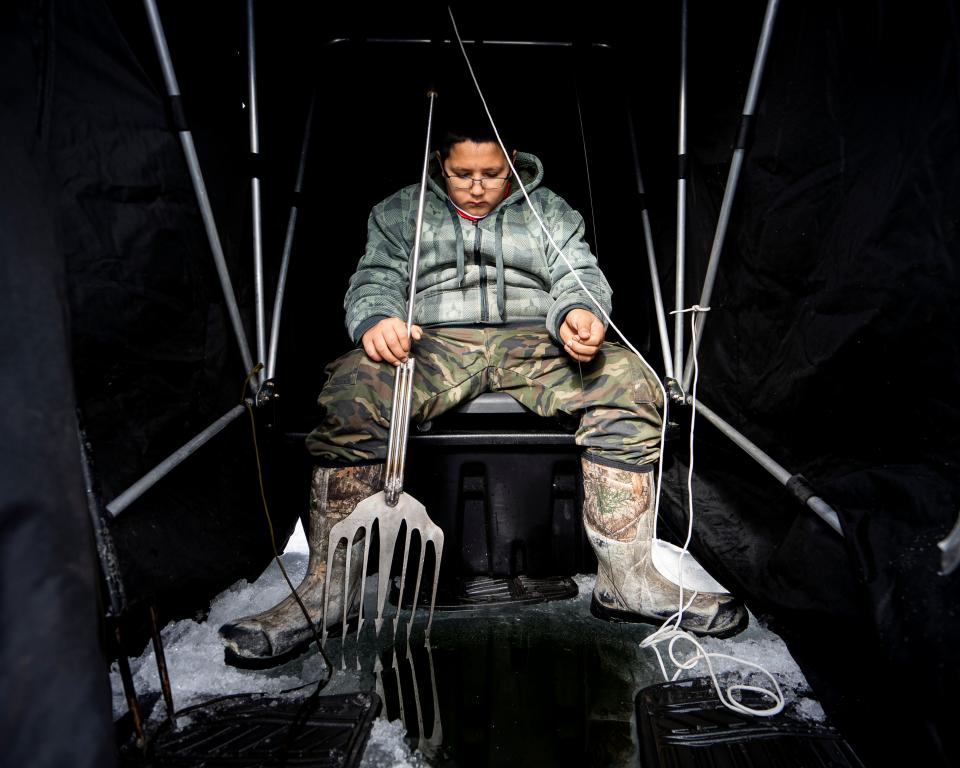 John Johnson III, 12, sits in an ice shelter as he waits to spearfish a musky during the Ishpaagoonika Deep Snow Camp at Pelican Lake on Jan. 28, 2024.