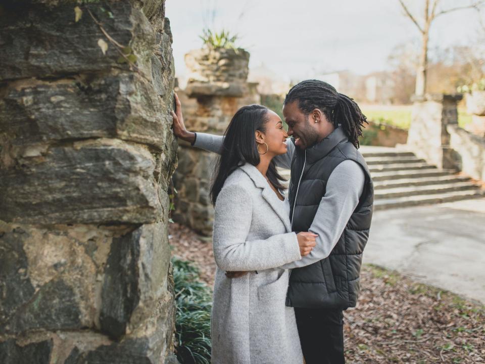 A couple hugs and leans their noses together as the groom puts a hand against a wall.