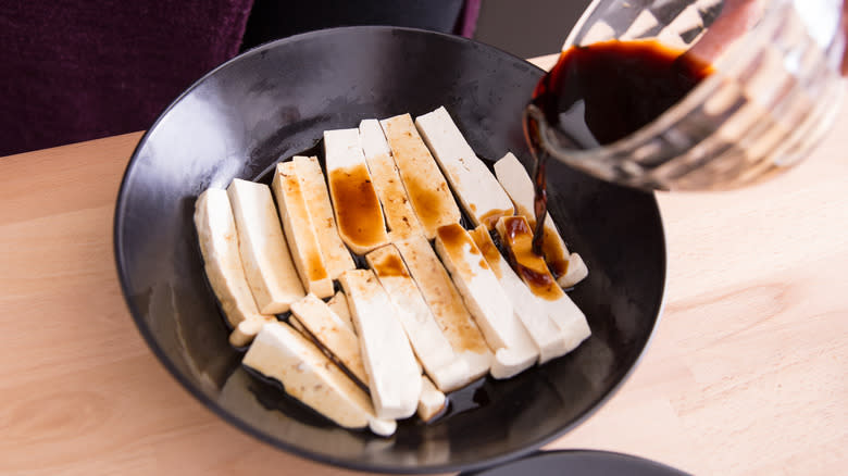Pouring a marinade over tofu strips