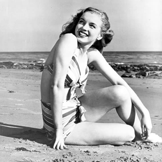 <p>Pre blonde hairdo, Monroe is seen lounging on the beach in a charming striped bikini with ties galore.</p>