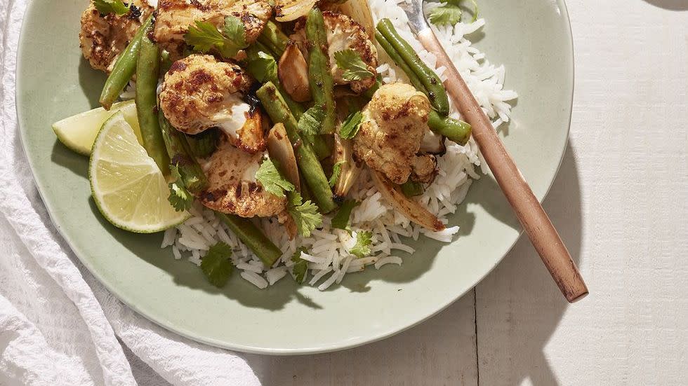 roasted curried cauliflower and green beans over white rice in a light green bowl with a fork