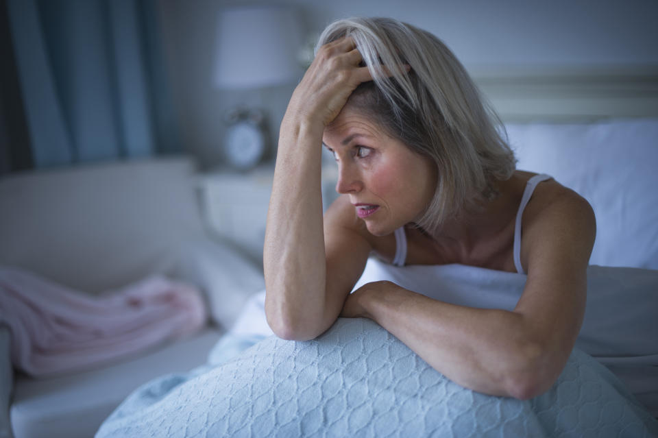 Woman sits up in bed looking tired and holding her head in her hands.