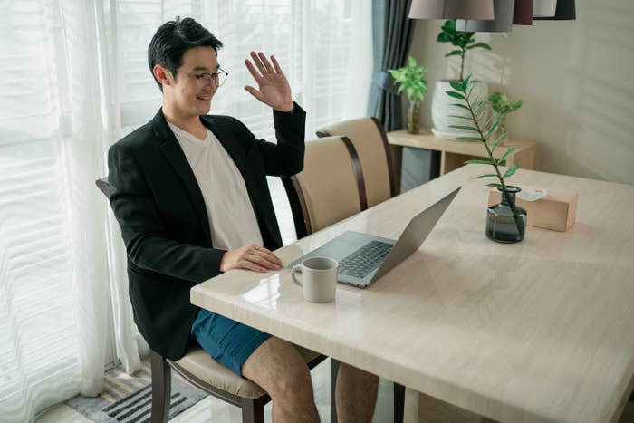 man signing on to a video call from home wearing a blazer on the top and boxers on the bottom