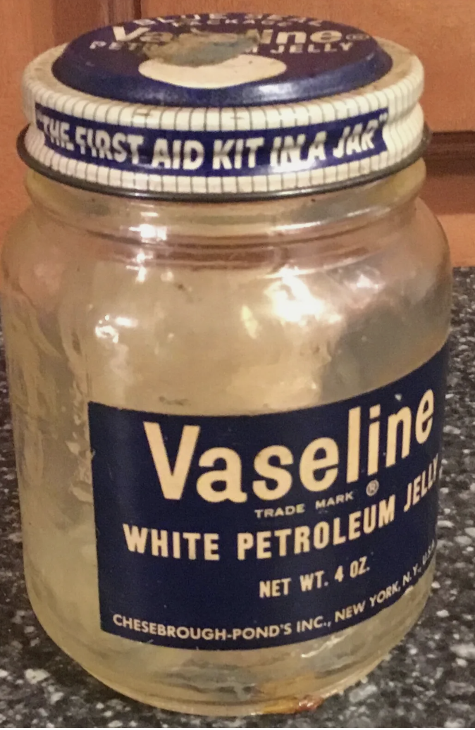 A vintage jar of Vaseline White Petroleum Jelly with the label "The First Aid Kit in a Jar" on the lid. The jar is 4 oz by Chesebrough-Pond's Inc