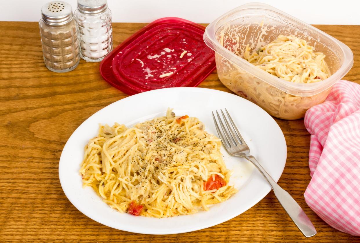 Helping of leftover chicken spaghetti from plastic bowl heated in microwave and served on white plate.