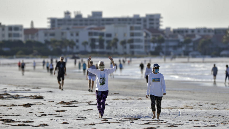 FILE - In this April 27, 2020, file photo, two women wearing safety masks stretch as they walk on Siesta beach in Siesta Key, Fla. As the weather warms, some already have begun venturing outside in larger numbers, despite guidance to stay home. Government officials say they aim to manage public health risks in a way that allows for a gradual return to normal, but with the course of the outbreak still unknown, nobody is sure what summer will bring. (AP Photo/Chris O'Meara, File)