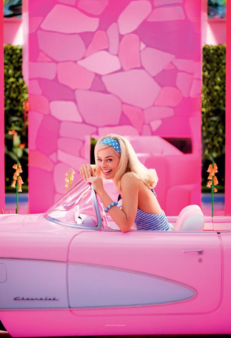 margot robbie, as barbie, sits in a pink car and smiles in a first look photo from the barbie movie