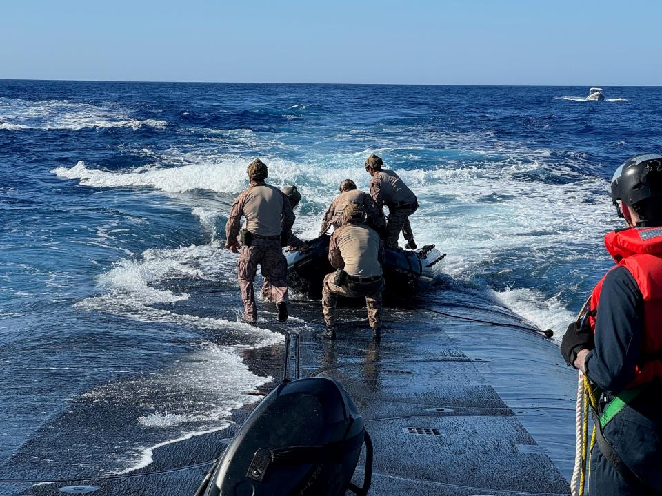 US Marines pull a small vessel out of the blue ocean onto the top of a US Navy submarine.