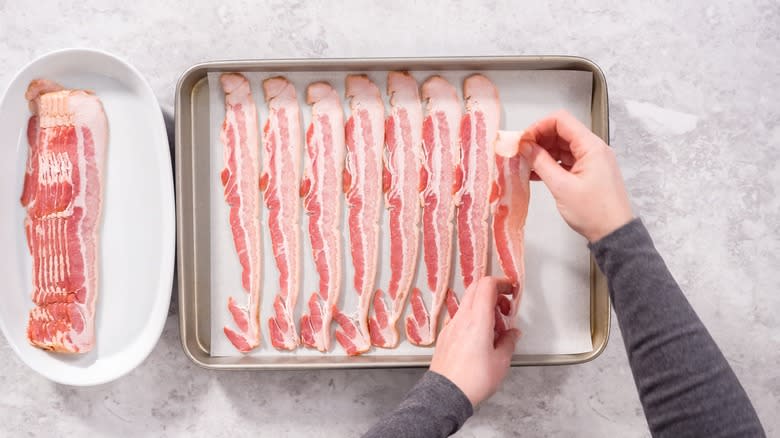 Raw bacon being placed onto sheet