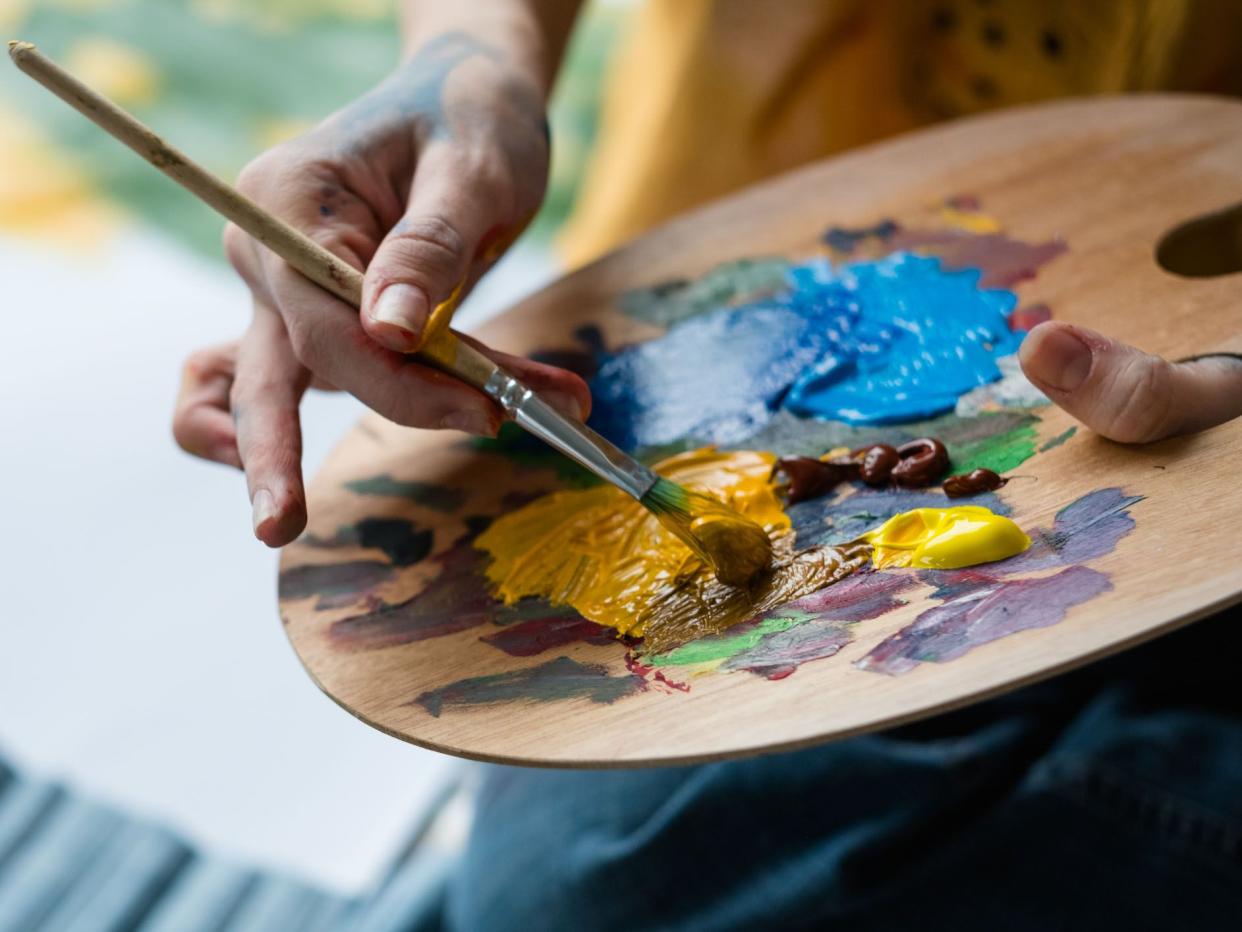 Fine art school. Closeup of artist hands holding wooden palette, mixing acrylic paint with brush.