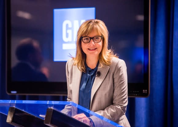 Barra is shown standing at a podium in front of a lighted GM logo.