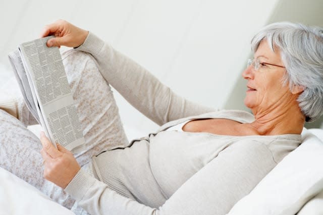 C4T88N Retired smiling senior woman reading newspaper on the bed at home