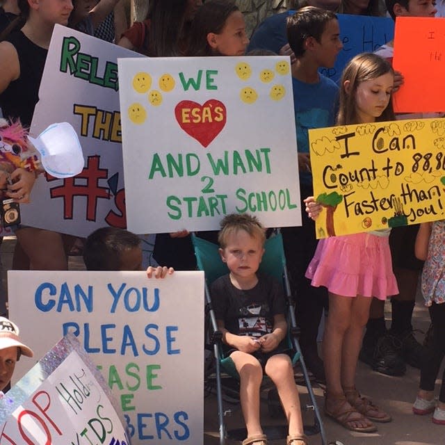 Parents and children hold signs on Sept. 30, 2022, in favor of ESA programs making private school efforts available to all.