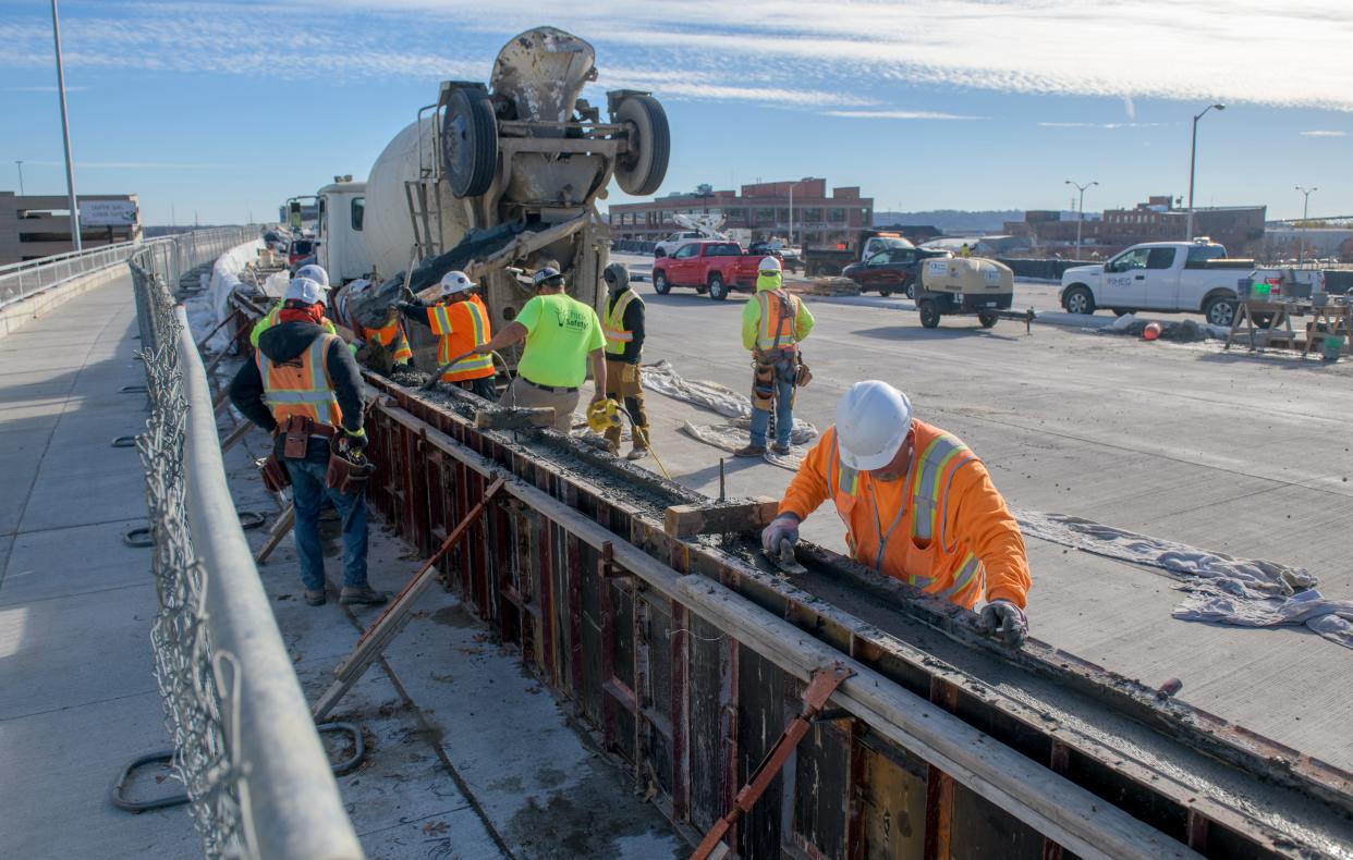 Workers build a concrete barrier between the pedestrian walkway and the westbound lanes of the Bob Michel Bridge.