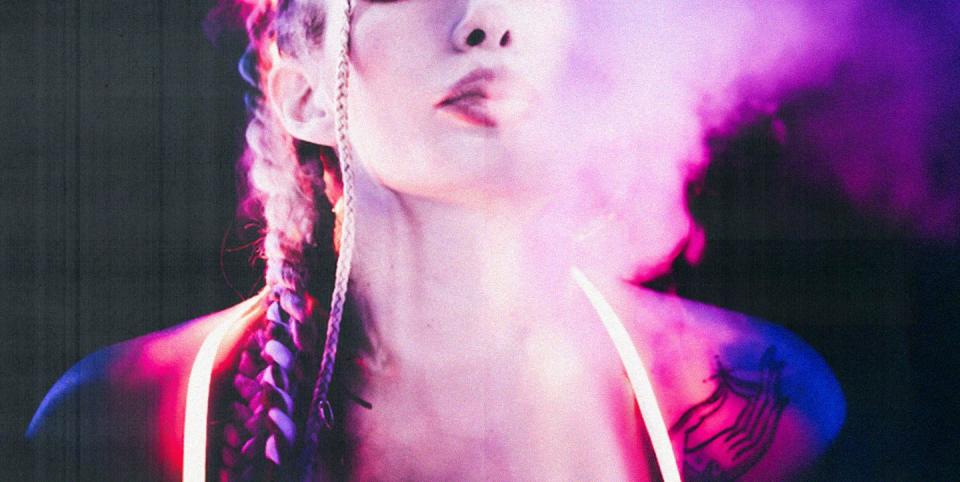 a woman bathed in purple light breathing smoke clouds out