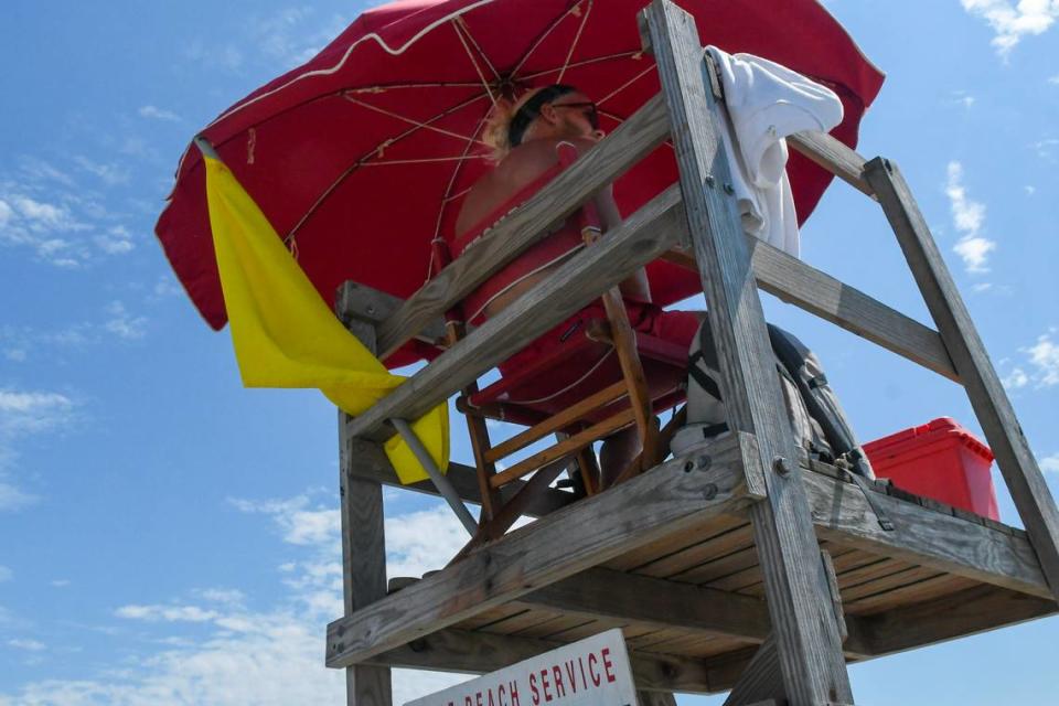 A Shore Beach Service lifeguard displays a yellow flag that warns beach goers of stronger than usual surf, including rip currents.