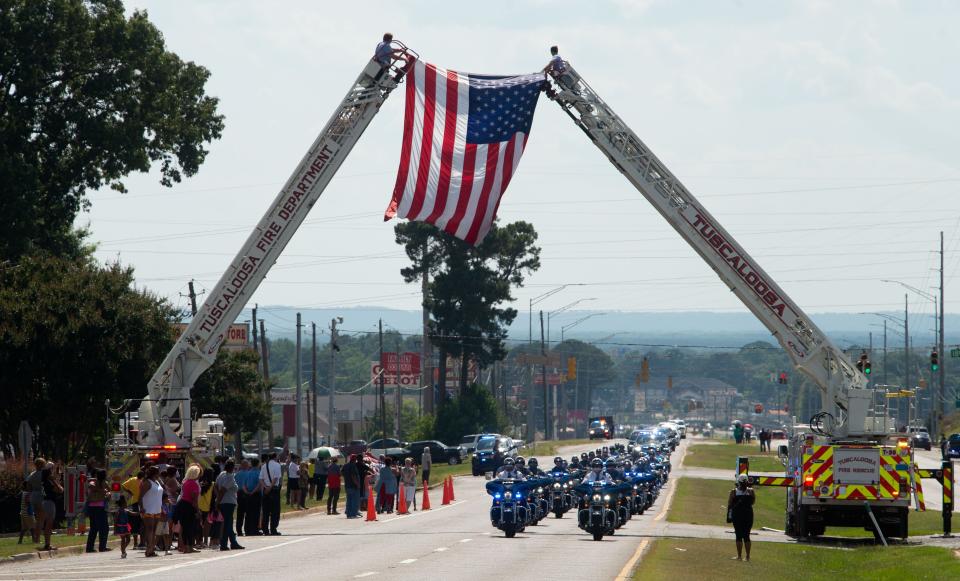 June 18, 2022; Tuscaloosa, AL, USA; Tuscaloosa honored the passing of Meridian Police Officer Kennis Croom, a native of Tuscaloosa, with a memorial service at Shelton State Community College. Two ladder trucks from Tuscaloosa Fire Rescue Service display a flag over Skyland Blvd. as the motorcade bearing Officer Croom’s body approach Memory Hills Garden for the burial. Gary Cosby Jr.-The Tuscaloosa News