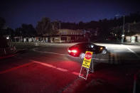 FILE - In this Oct. 10, 2019 file photo a car drives through a darkened Montclair Village as Pacific Gas & Electric power shutdowns continue in Oakland, Calif. California regulators are voting Wednesday, Nov. 13, on whether to open an investigation into pre-emptive power outages that blacked out large parts of the state for much of October as strong winds sparked fears of wildfires. The state’s largest utility, Pacific Gas & Electric Co., initiated multiple rounds of shut-offs that plunged nearly 2.5 million people into darkness throughout northern and central California. (AP Photo/Noah Berger, File)