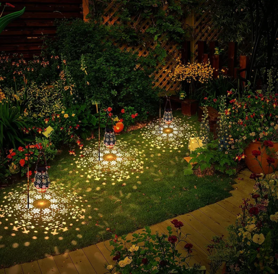 High-angle view of backyard at night with colorful flowers and hanging lanterns casting snowflake patterns onto the lawn