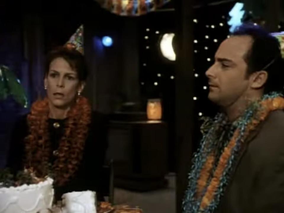 janet and ned sitting at a table with party hats and leis in "house arrest"