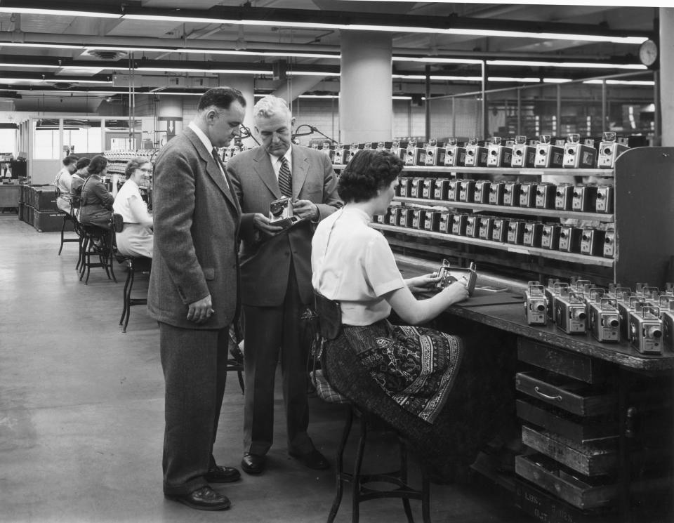 A line of female employees work on an assembly line for the Eastman Kodak Brownie camera, as two male supervisors inspect one of the cameras, circa 1945. The finished cameras line shelves above the bench. (Hulton Archive / Getty Images)