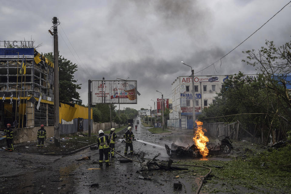 Rescue workers put out the fire of a destroyed car after a Russian attack in a residential neighborhood in downtown Kharkiv, Ukraine, on Monday, July 11, 2022. The top official in the Kharkiv region said Monday the Russian forces launched three missile strikes on the city targeting a school, a residential building and warehouse facilities. (AP Photo/Evgeniy Maloletka)