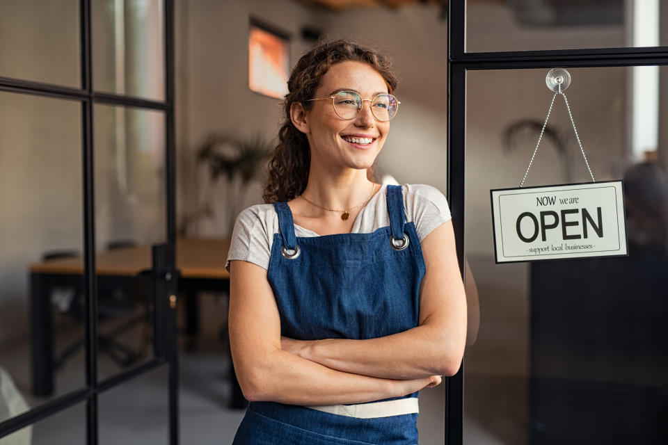 Portrait of smiling female business owner standing at restaurant entrance while looking outdoors. 