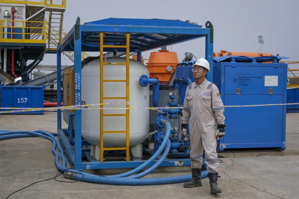 FILE - A Chinese worker from China Oilfield Services Limited (COSL), a contractor for China National Offshore Oil Corporation (CNOOC), stands by machinery next to the drilling rig at the Kingfisher oil field on the shores of Lake Albert in the Kikuube district of western Uganda, Jan. 24, 2023. Uganda National, which owns part of the Kingfisher project, was among companies whose plans for renewable energy were aimed primarily at using the clean power to decarbonize its fossil fuel projects, not replace them with cleaner pursuits. (AP Photo/Hajarah Nalwadda, File)