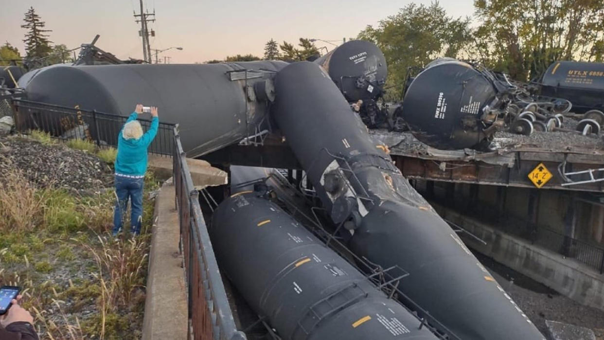 A resident senior takes a photo of a half-dozen huge cylinders piled up after a derailment.