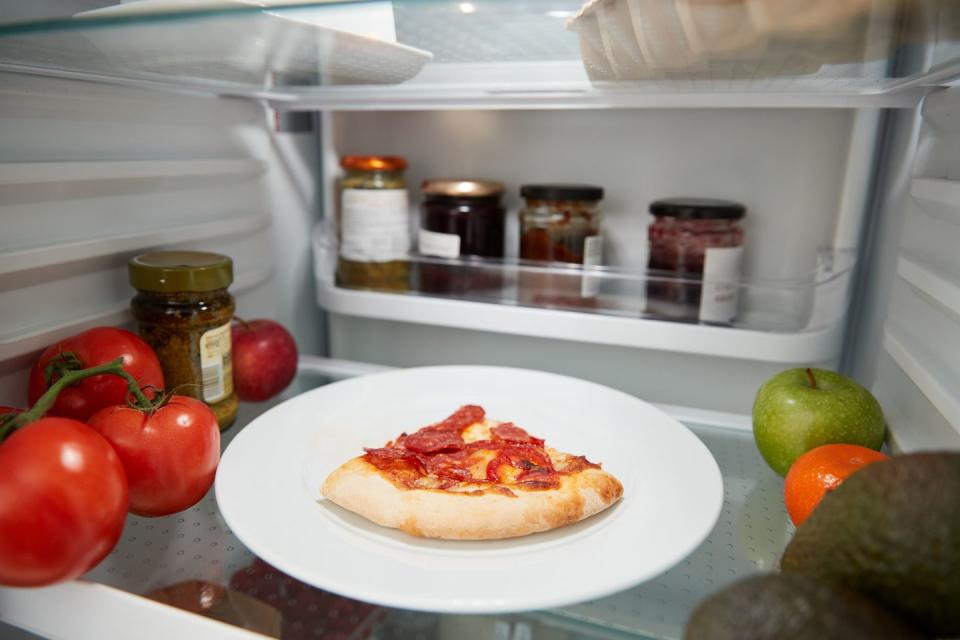 view inside refrigerator of leftover takeaway pizza slice on shelf