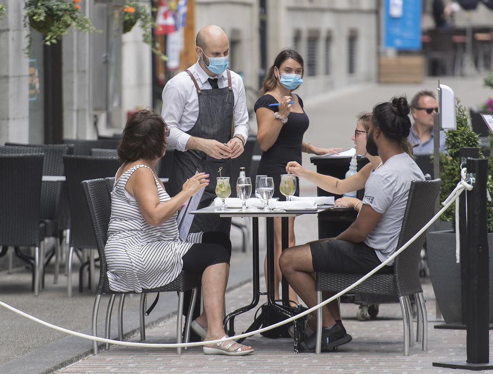 Servers wear face masks as they take orders at an outdoor terrace in Montreal, Sunday, July 26, 2020, as the COVID-19 pandemic continues in Canada and around the world. (Graham Hughes/The Canadian Press via AP)