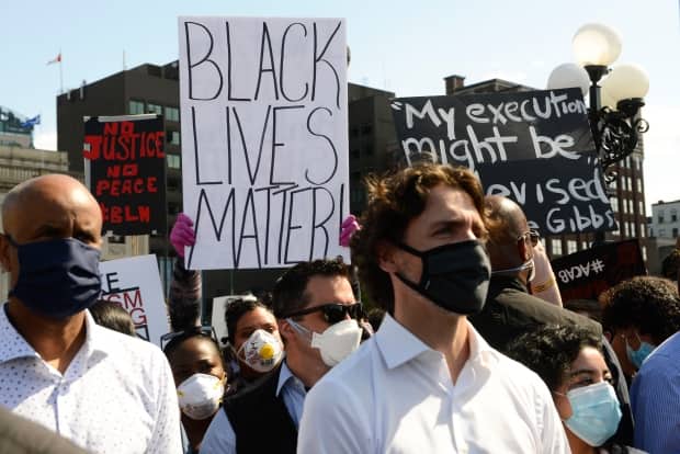 A protester holds up a Black Lives Matter sign behind Prime Minister Justin Trudeau as people take part in an antiracism protest on Parliament Hill in Ottawa on Friday, June 5, 2020.