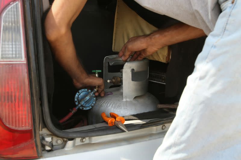 Moises Vilchez connects a cooking gas canister on the trunk of his car, which is used to run his vehicle instead of fuel, as Venezuelans are struggling to cope with chronic fuel shortage, in Maracaibo