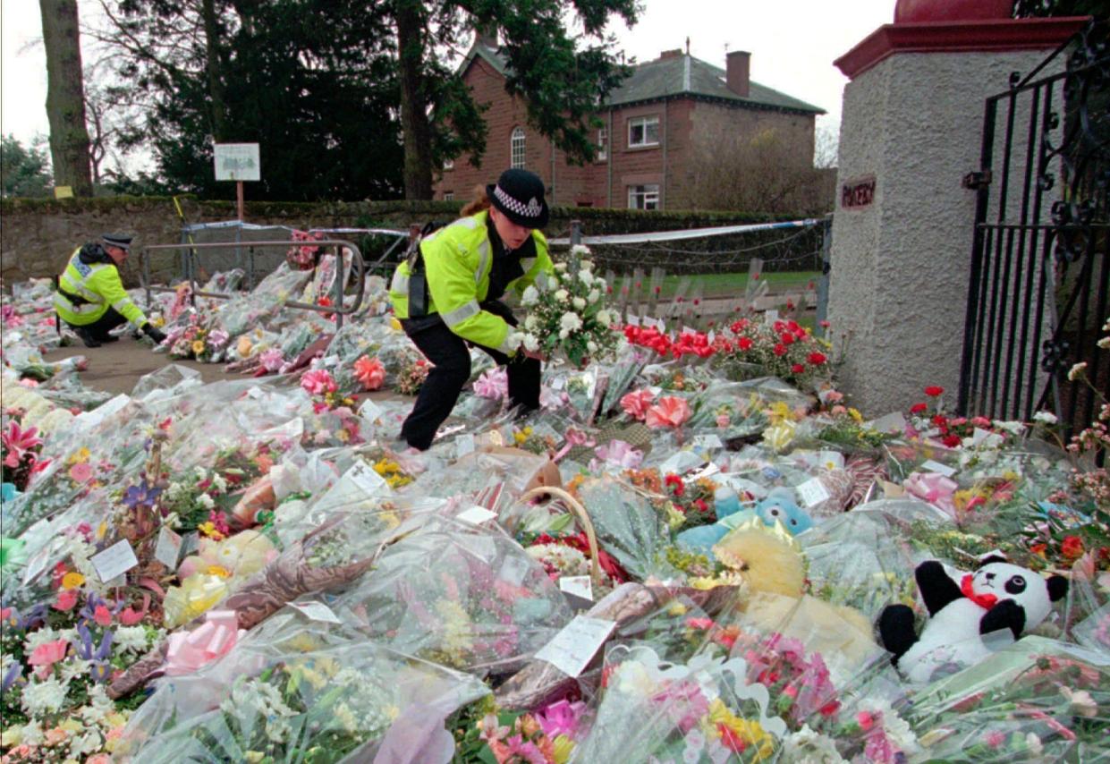 A police officer arranges bouquets of flowers in rows at a side entrance to Dunblane Primary School in Dunblane, Scotland, on March 15, 1996. One of Britain's deadliest mass shootings took place at the school.
