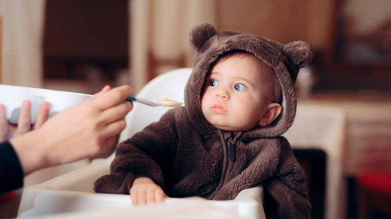 baby leans away from food spoon